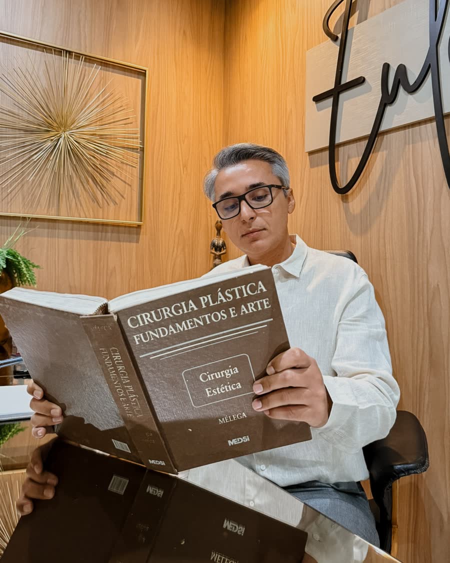 Dr. Euler Amaral à mesa, de óculos, lendo um livro de cirurgia plástica