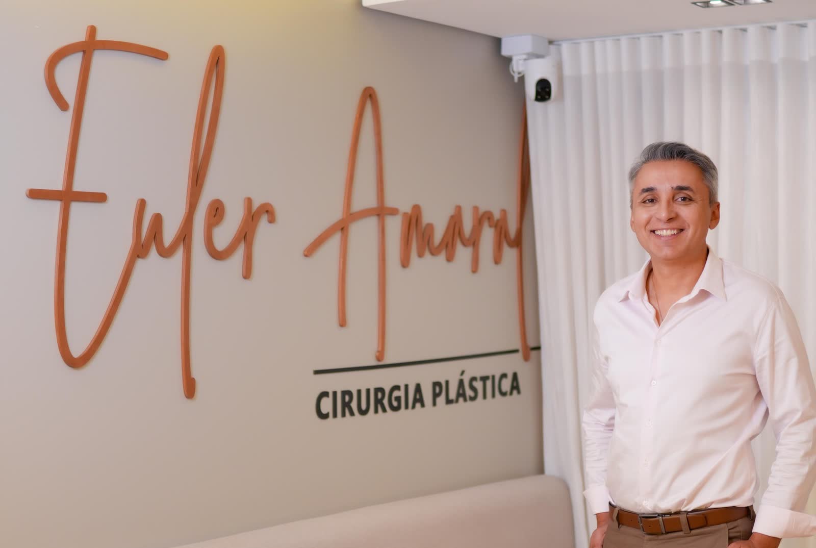 Recepção do consultório, com o letreiro Euler Amaral Cirurgia Plástica e o Dr. Euler em pé ao lado