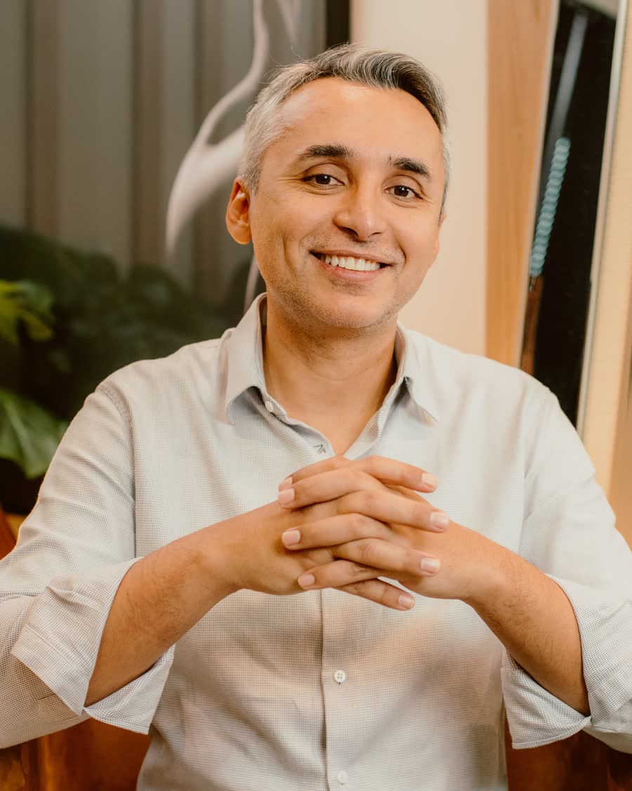 Dr. Euler Amaral sorrindo, de camisa clara, com as mãos entrelaçadas